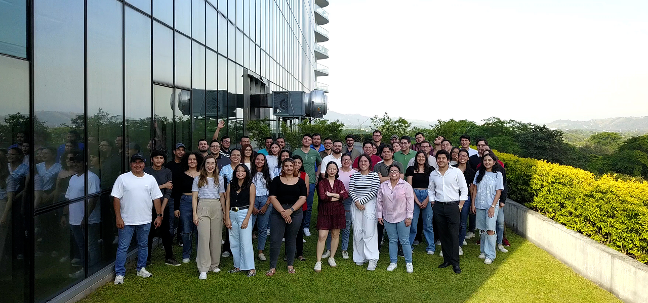 Roughly 50 Work Ninjas team members on a rooftop terrace, glass office tower behind them